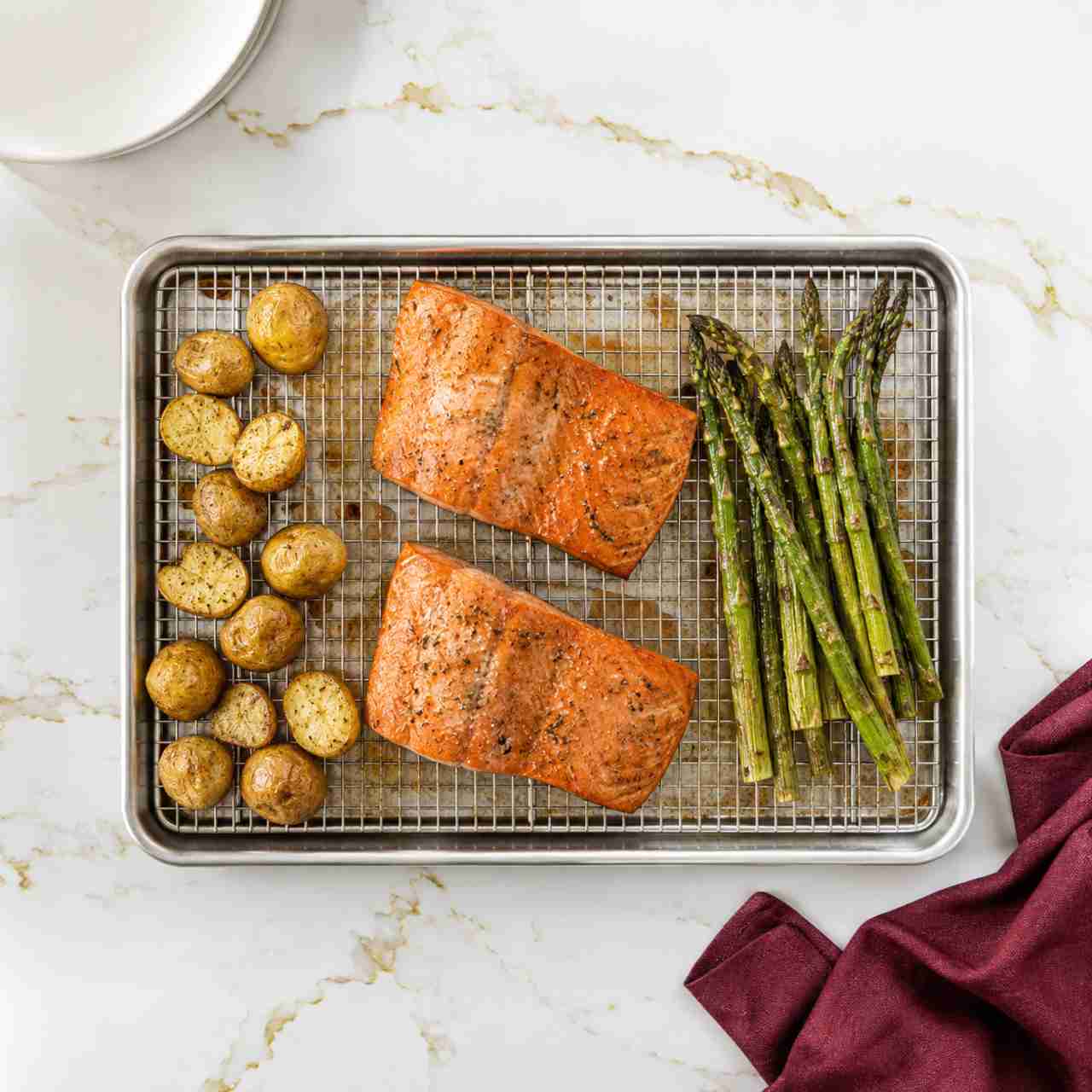 An overhead view of a cooling rack in a sheet pan with roasted salmon, asparagus, and potatoes.
