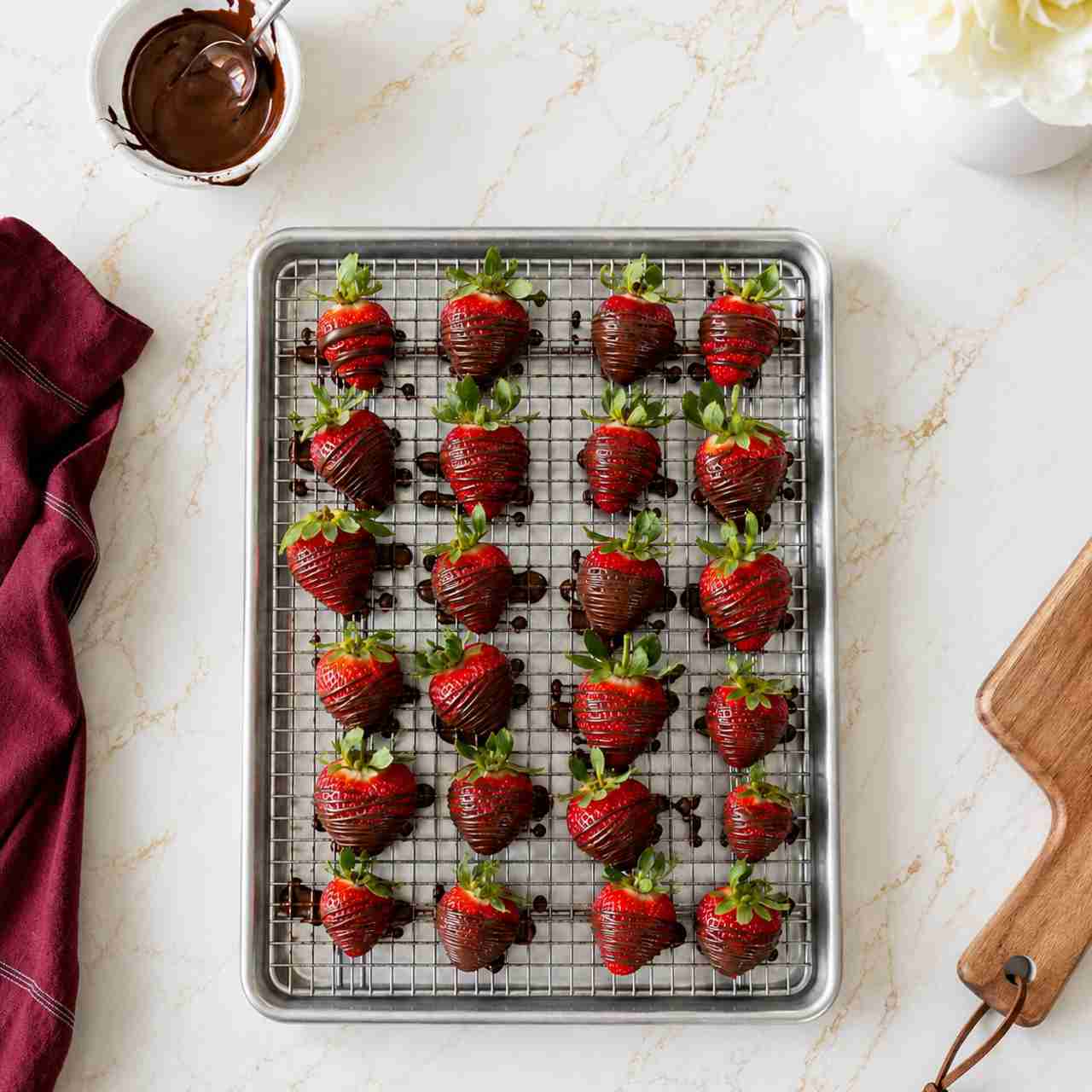 An overhead view of chocolate drizzled strawberries on a cooling rack on a sheet pan to catch the excess chocolate.