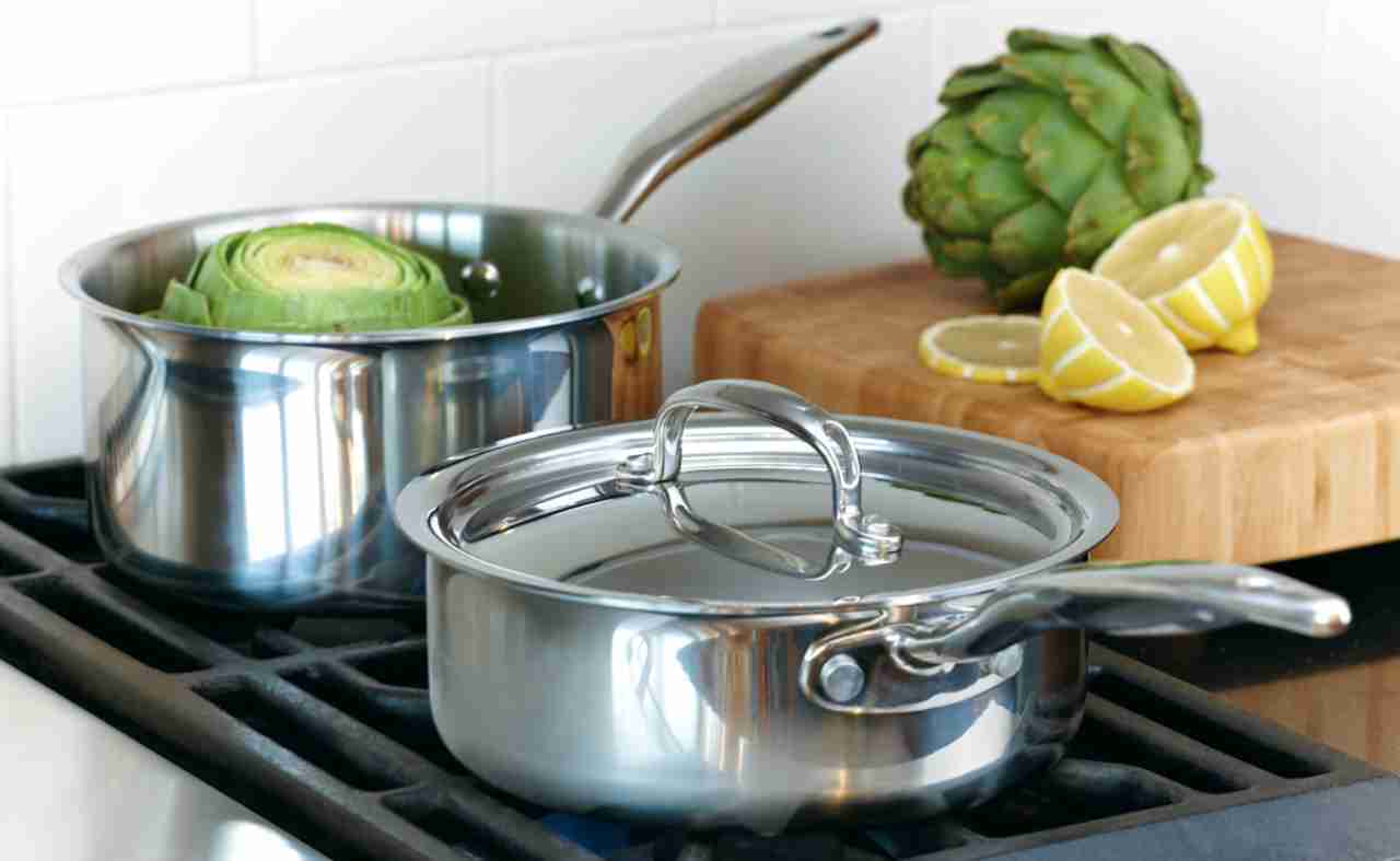 Two Heritage Steel Titanium Series sauce pans on a stovetop with artichokes and lemons