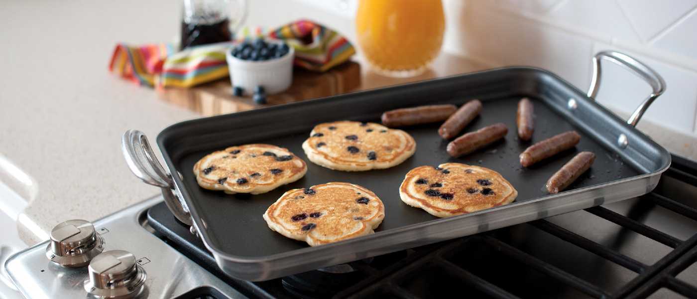 The Nordic Ware high-sided griddle on a stovetop cooking pancakes and sausage