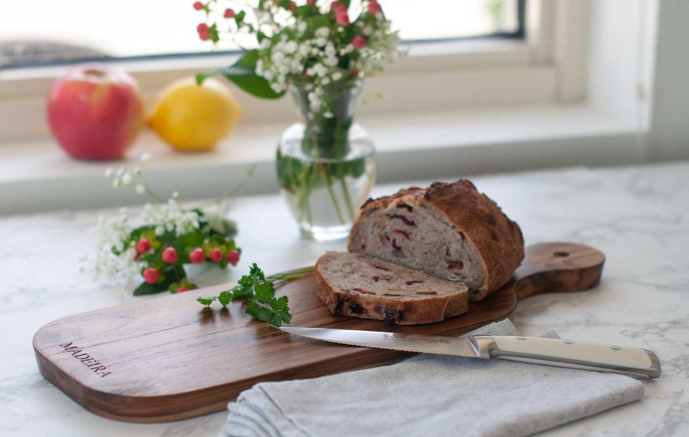 A teak bread board on a kitchen counter with sliced bread