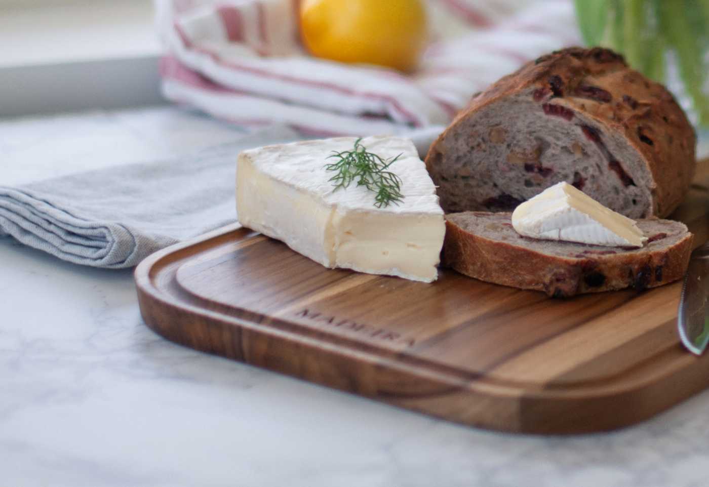 A teak cutting board with bread and brie